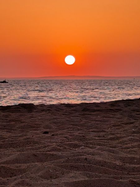 A vibrant orange sunset illuminates the sky over a calm sea and sandy beach. Faro Portugal 🇵🇹